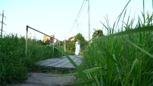 Young woman in the white dress crossing bridge on nature