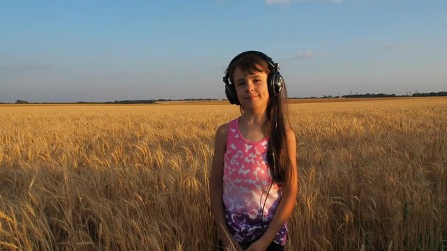 A girl on a wheat field listening to music on headphones. A child dances in headphones on a wheat field.