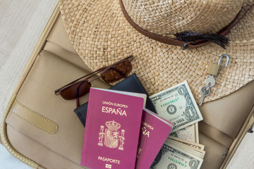 Tourism travel concept. Suitcase with female hat, sunglasses, spanish passports, dollars and padlock