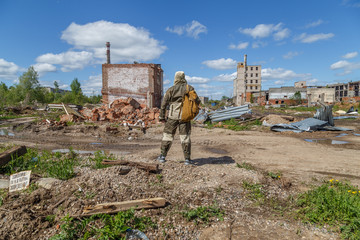A man with a backpack in military uniform on the background of a destroyed building