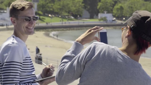 Man Takes A Photo Of His Partner Drawing On A Tablet At The Beach In San Francisco 