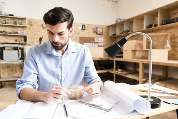Concentrated youthful timber craftsman creating new sketches in workshop