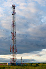 Telecommunication antenna tower on a background of clouds in the sky. Evening, sunset