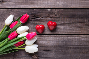 Two red decorative hearts  and bright  spring  tulips flowers on rustic wooden background.