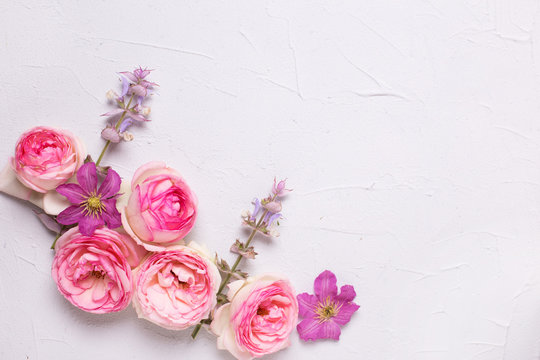 Pink roses and violet summer clematis flowers on grey textured background.