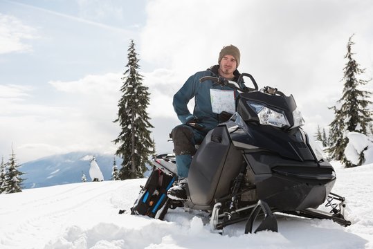Man holding a map while sitting on snowmobile in snowy alps