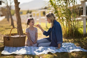 Mother feeding food to her daughter on picnic 