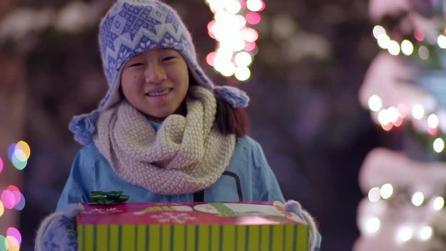 Bundled Up Little Girl Holds A Christmas Gift And Smiles (Slow Motion)