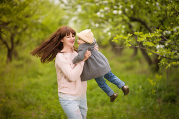 Obraz premium Beautiful young mother and daughter are walking laughing to have fun in the green spring or summer garden or park, family walk