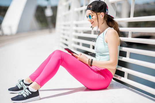Young woman in bright sportswear resting outdoors during the training on the modern white bridge in Lyon city