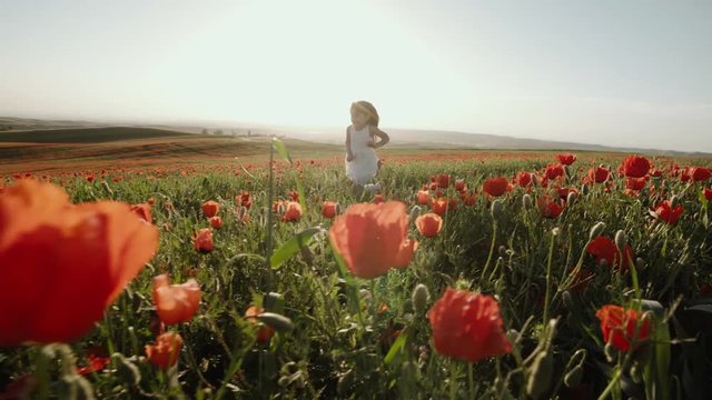 little Asian girl in a white dress running through field of red poppies slow motion, sunset