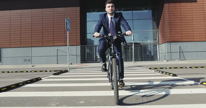 Businessman in a suit riding a bike through a pedestrian crossing in time his morning travel to job.