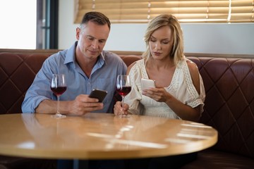 Couple using mobile phones while having glass of wine