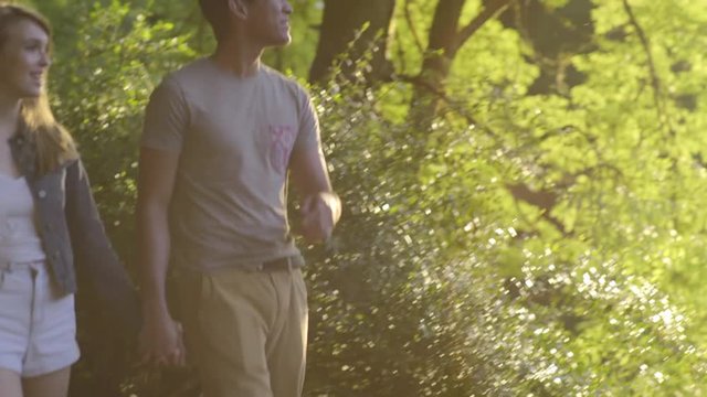 Couple Walk Along Path, Young Man Takes A Photo Of His Girlfriend In Front Of A Pond 