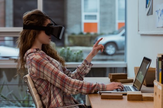 Female executive using virtual reality headset while working on laptop at desk