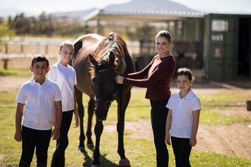 Happy family standing with a brown horse in the ranch