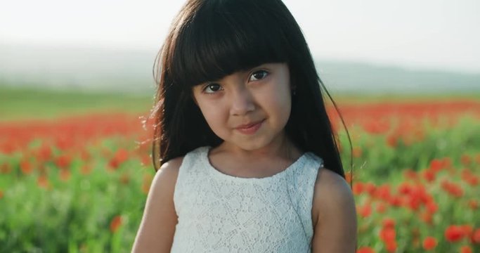 close-up portrait of a little Asian girl in white dress in field of red poppies on a Sunny spring day