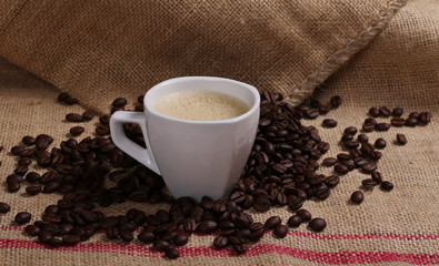 White cup and coffee beans on jute background, texture