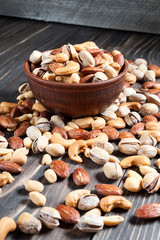 Mixed nuts spilling out of bowl on wooden table. Macro still-life with shallow dof