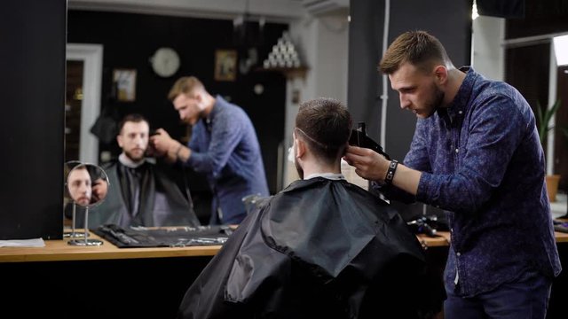 Man looking at reflection sitting in barbershop while master making hair