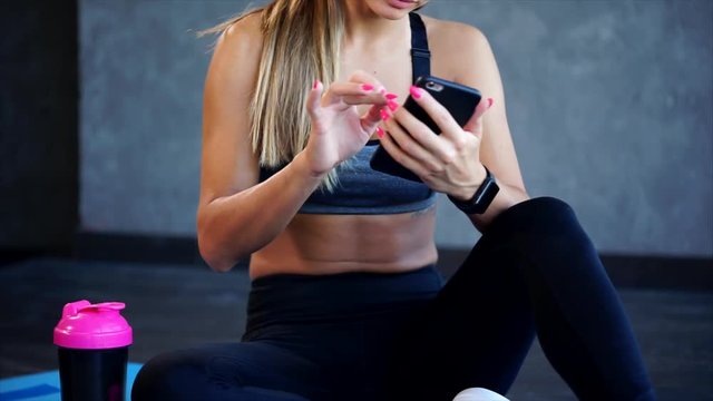 Woman in the gym after the exercises. She typing on the smartphone. Close up view