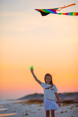 Little girl with flying kite on tropical beach at sunset. Kid play on ocean shore. Child with beach toys.