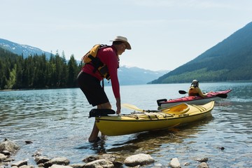 Man holding kayak while woman kayaking in lake