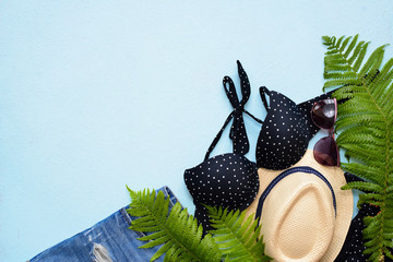 Female summer bikini swimsuit and accessories collage on blue with palm branches, hat and sunglasses.