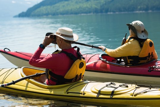 Man using binoculars while kayaking with woman