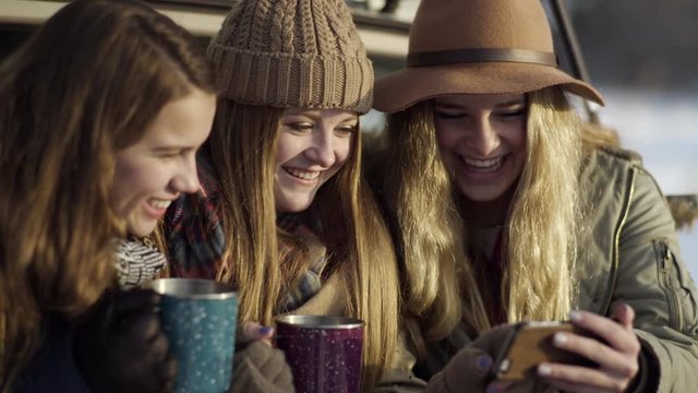 Group Of Fun Teen Girls Sit In Back Of Car And Scroll Through Funny Photos On Phone, They Laugh
