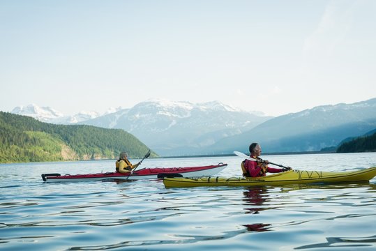 Side view of couple kayaking on lake against sky