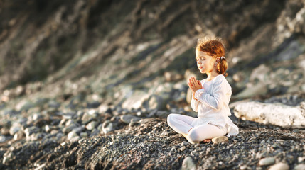 Happy child girl meditates in lotus position, engaged in summer yoga