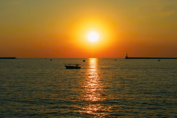 Naklejka na ściany i meble Lonely boat in the sea under sunset sky near lighthouse