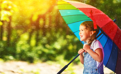 Happy child girl laughs and plays under summer rain with an umbrella