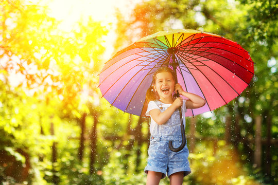 Happy child girl laughs and plays under summer rain with an umbrella