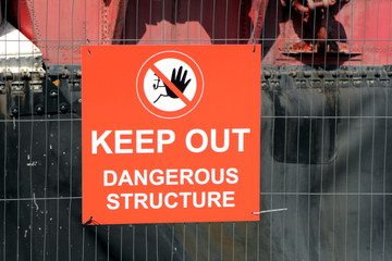 Sign on wire fence saying "Keep Out Dangerous Structure" with hand icon