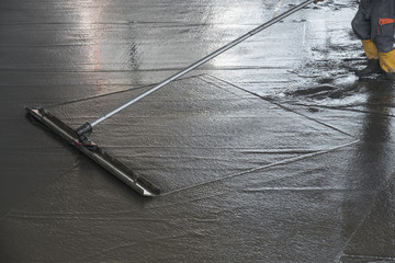 Worker leveling fresh poured concrete floor with a channel float