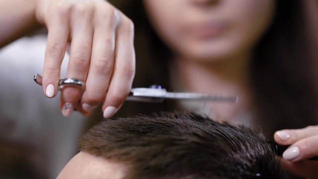 Unrecognizable hairdresser woman cutting hair to the customer with scissors