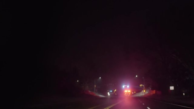 Driver's Perspective Of Fire Engine With Flashing Lights, Driving Through Empty Intersection, On Road In Winter At Night