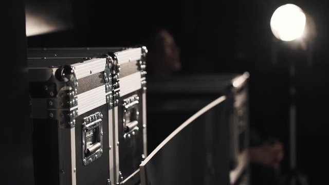 Metal black boxes with scenery equipment at theatre dark storage room with spotlight and sitting man in corner