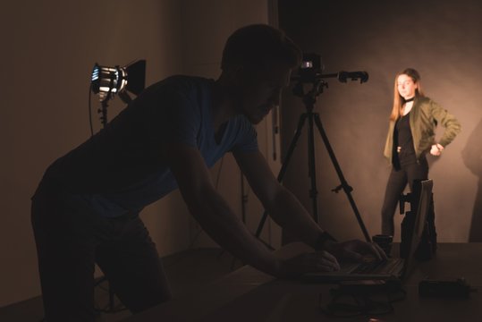 Man using laptop with female model standing by backdrop