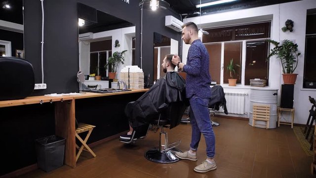 Side view of master combing hair to male customer in barber shop