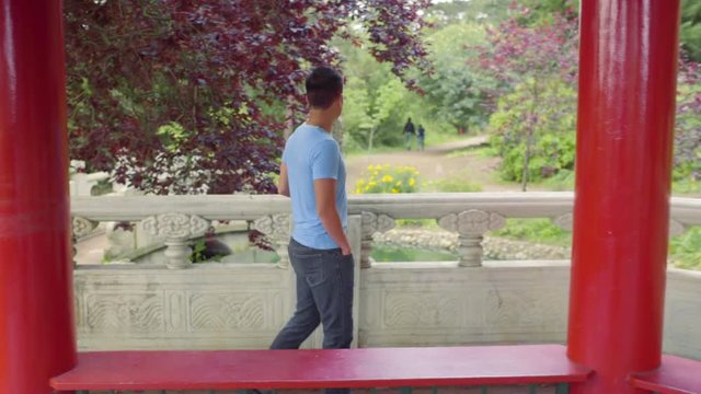 Man Enjoys Walking Around A Red Pagoda, Looks Out At Garden 