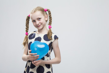 Portrait of Funny Caucasian Blond Girl With Pigtails Posing in Polka Dot Dress Against White. Holding Blue Air Balloon.