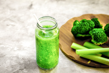 Green vegetable smoothie in glass at gray background