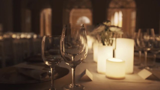 Clean wine glasses on dinner table with warm light lit wax candles and plates at banquette dining hall