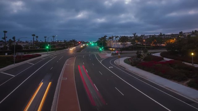 Time-lapse or hyper-lapse in Newport Beach over the Pacific Coast Highway or PCH with traffic below and clouds above. Shot at sunset with traffic, car lights, homes and street lights in the back