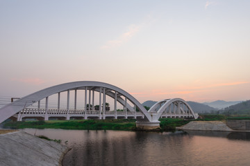 Fototapeta na wymiar The white bridge backdrop orange sky at the morning in Lamphun. Thailand