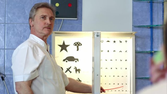 Elderly male ophthalmologist pointing at letters of eye chart