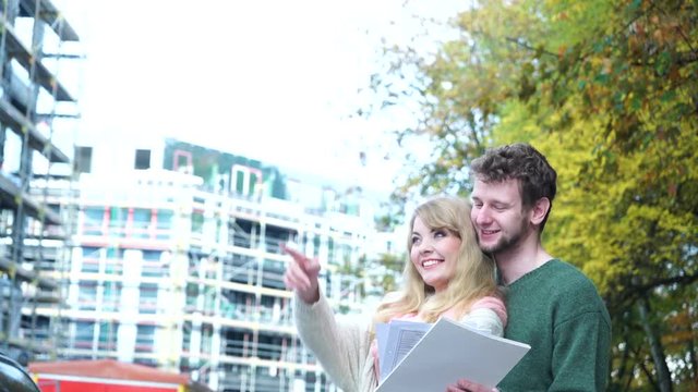 Real estate family and housing development concept - young couple on front of new big modern house construction site with blueprint project dreaming about home 4K ProRes HQ codec